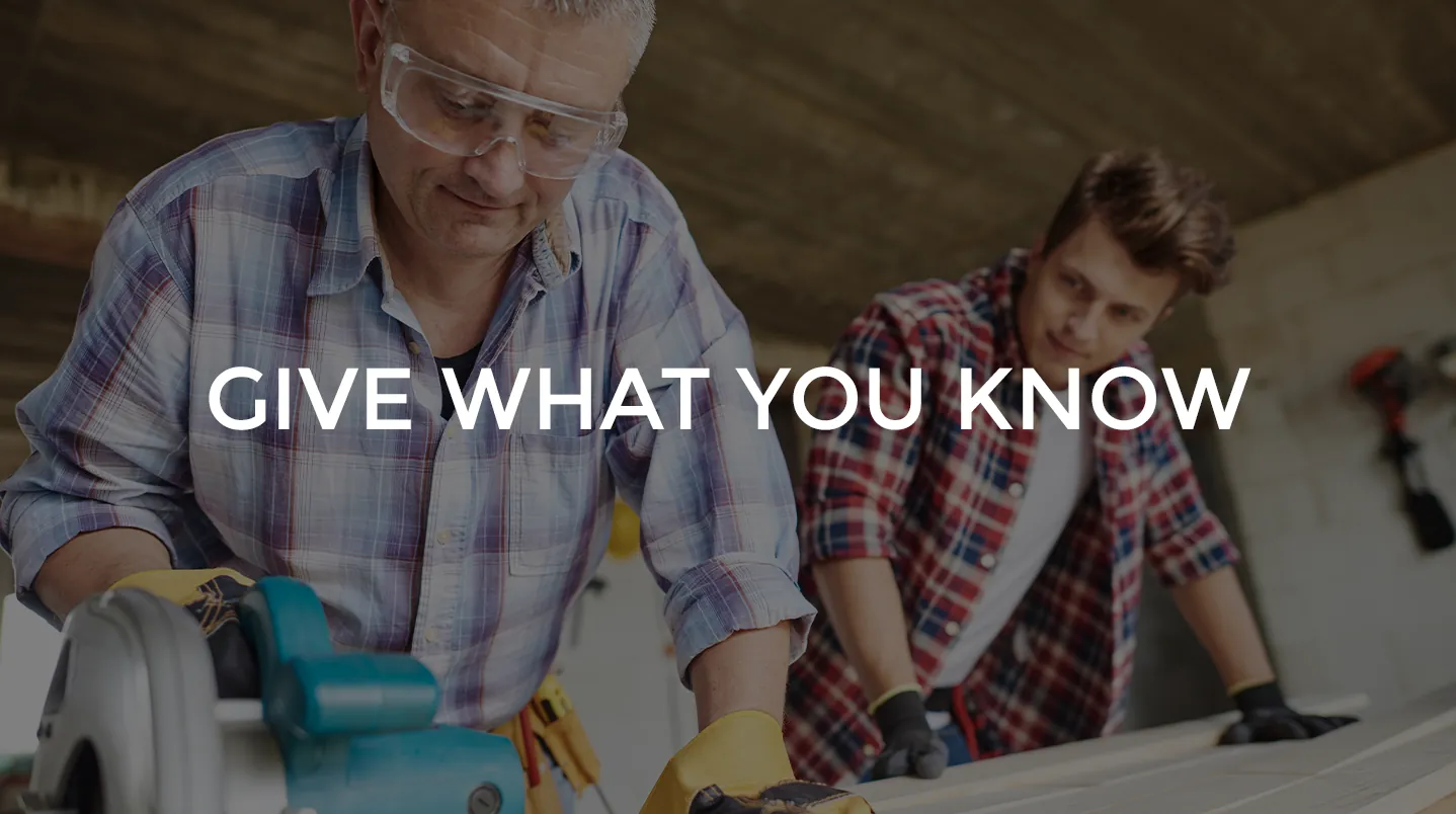 A man teaching a younger man woodworking at a workbench